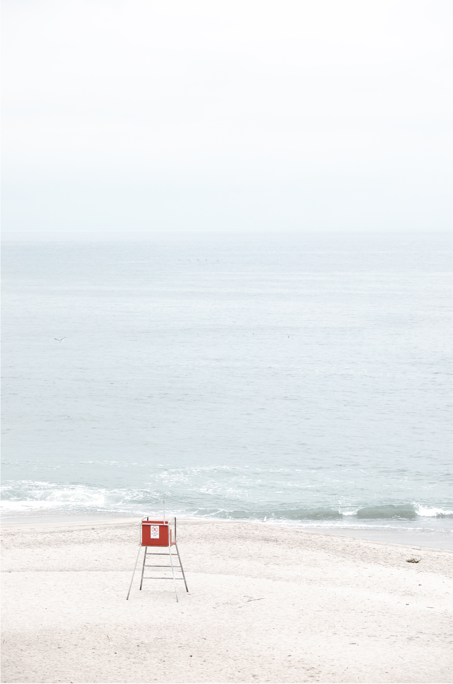 Vertical coastal photography featuring a red and white lifeguard chair and a calm ocean background, located in Laguna California.