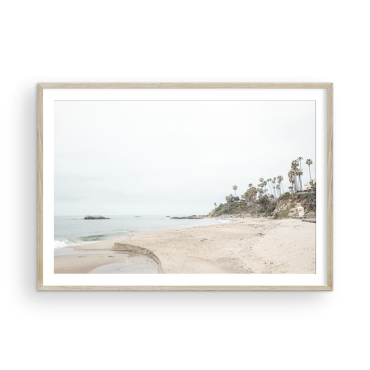 Horizontal coastal photography of a white lifeguard tower at Laguna Beach, California, depicting a beach scene with palm trees and a calm ocean. Photograph in minimalist mock up.
