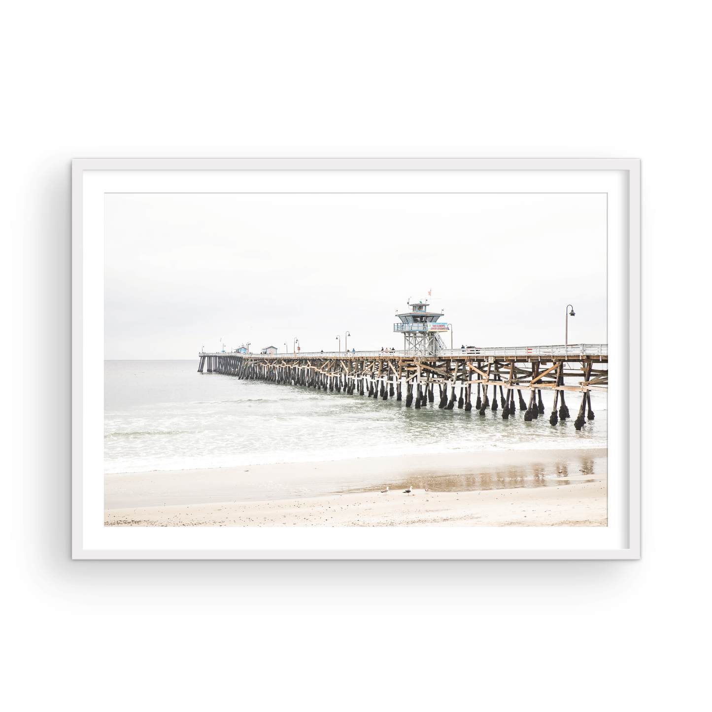A long wooden pier, the San Clemente Pier, extends into the ocean in this landscape coastal photography. The beach in the foreground suggests a calm ocean print, ideal for a large coastal wall art or a beach cottage wall decor. Photograph in minimalist mock up.