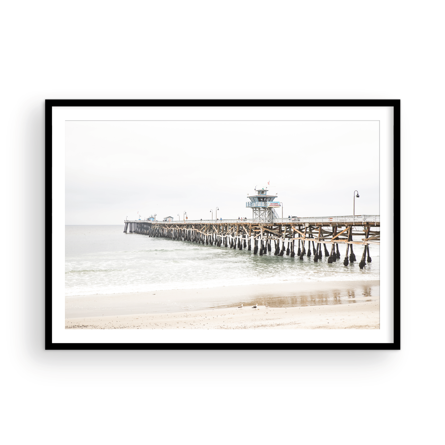 A long wooden pier, the San Clemente Pier, extends into the ocean in this landscape coastal photography. The beach in the foreground suggests a calm ocean print, ideal for a large coastal wall art or a beach cottage wall decor. Photograph in minimalist mock up.