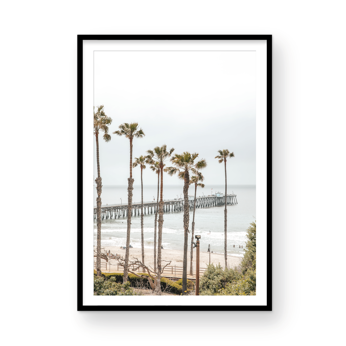 A vertical landscape coastal photography shot of the San Clemente Pier from behind a lush line of tall palm trees. This beachscape print highlights the California coast and is ideal for large beach art or a beach theme wall decor, with subtle ocean waves. Photograph in minimalist mock up.