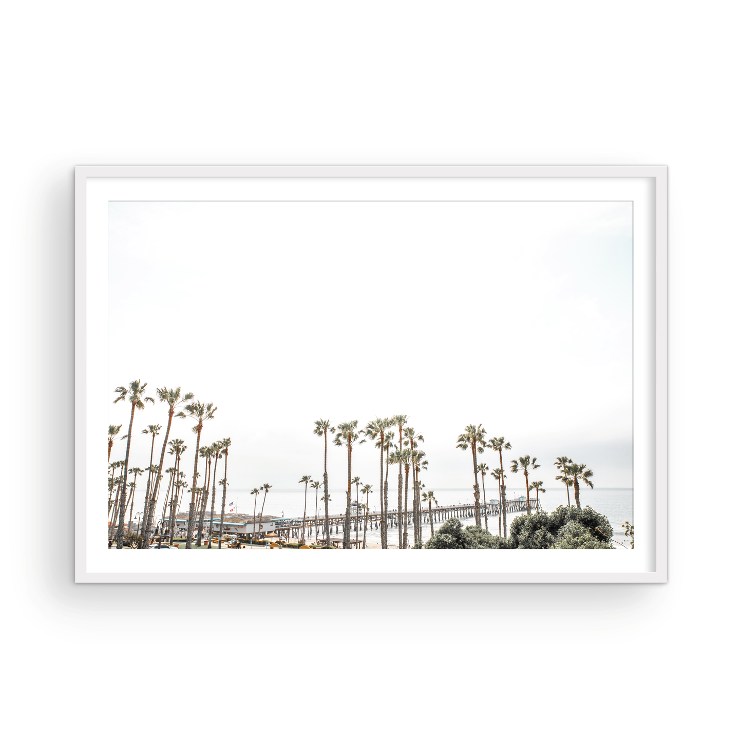 Horizontal landscape coastal photography of many palm trees in the foreground, with the San Clemente Pier extending into the ocean in the background. This large landscape beach art conveys strong beach vibes. Photograph in minimalist mock up.