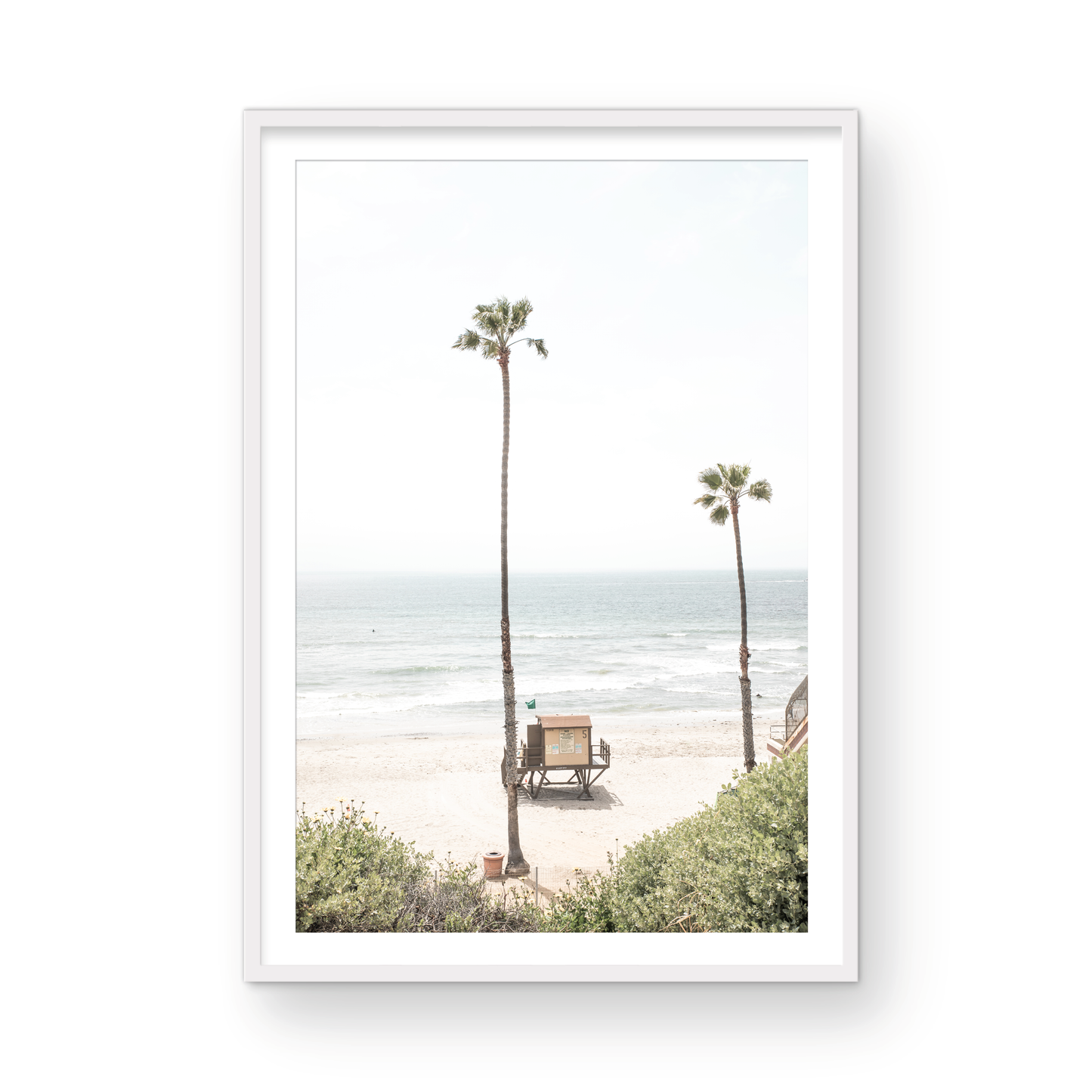 Vertical beach wall art featuring a lifeguard tower nestled between two tall palm trees on a sunny California beach, capturing a serene beach vibe. Photograph in minimalist mock up.