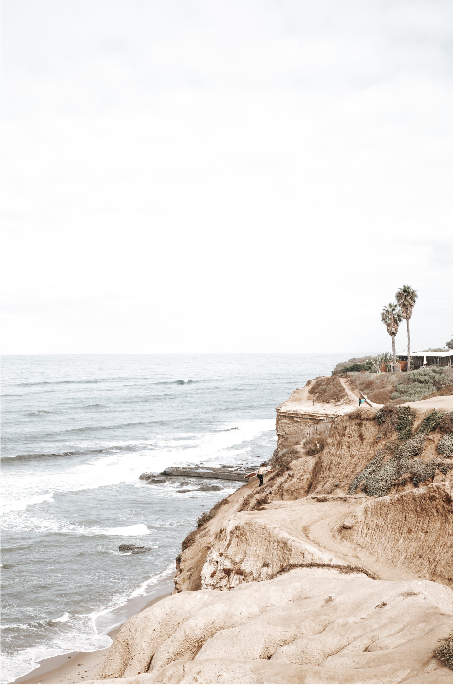 Fine art of Sunset Cliffs, San Diego California vertical print of hazy high-angle landscape beach photography captures a light blue ocean meeting tall tan and brown cliffs rise as iconic coastal scenery.