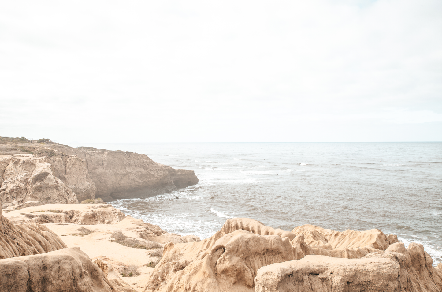Fine art of Sunset Cliffs, San Diego California horizontal print of hazy high-angle landscape beach photography captures a light blue ocean meeting tall tan and brown cliffs rise as iconic coastal scenery.