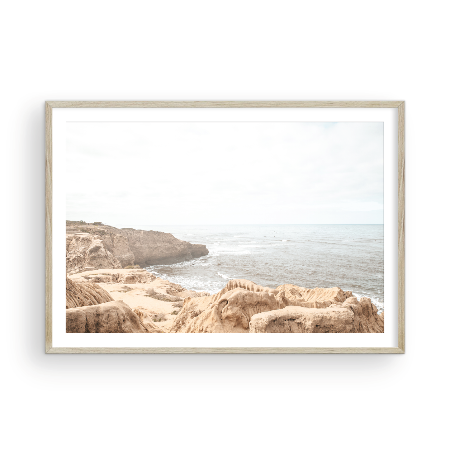 Fine art of Sunset Cliffs, San Diego California horizontal print of hazy high-angle landscape beach photography captures a light blue ocean meeting tall tan and brown cliffs rise as iconic coastal scenery. Photograph in minimalist art mock up.