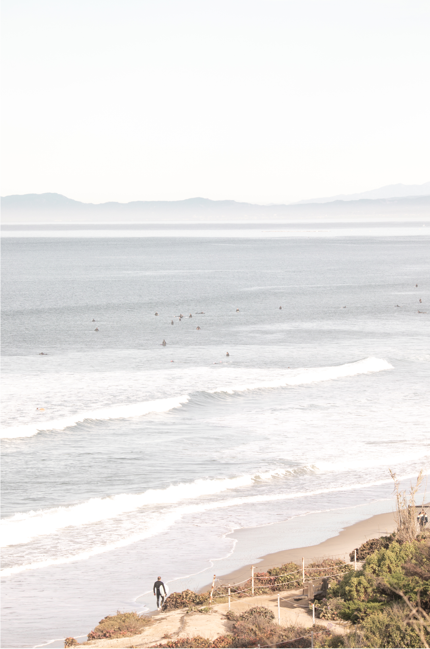 Minimalist ocean print of ocean waves with surfers in the distance and a sandy hillside in the foreground.