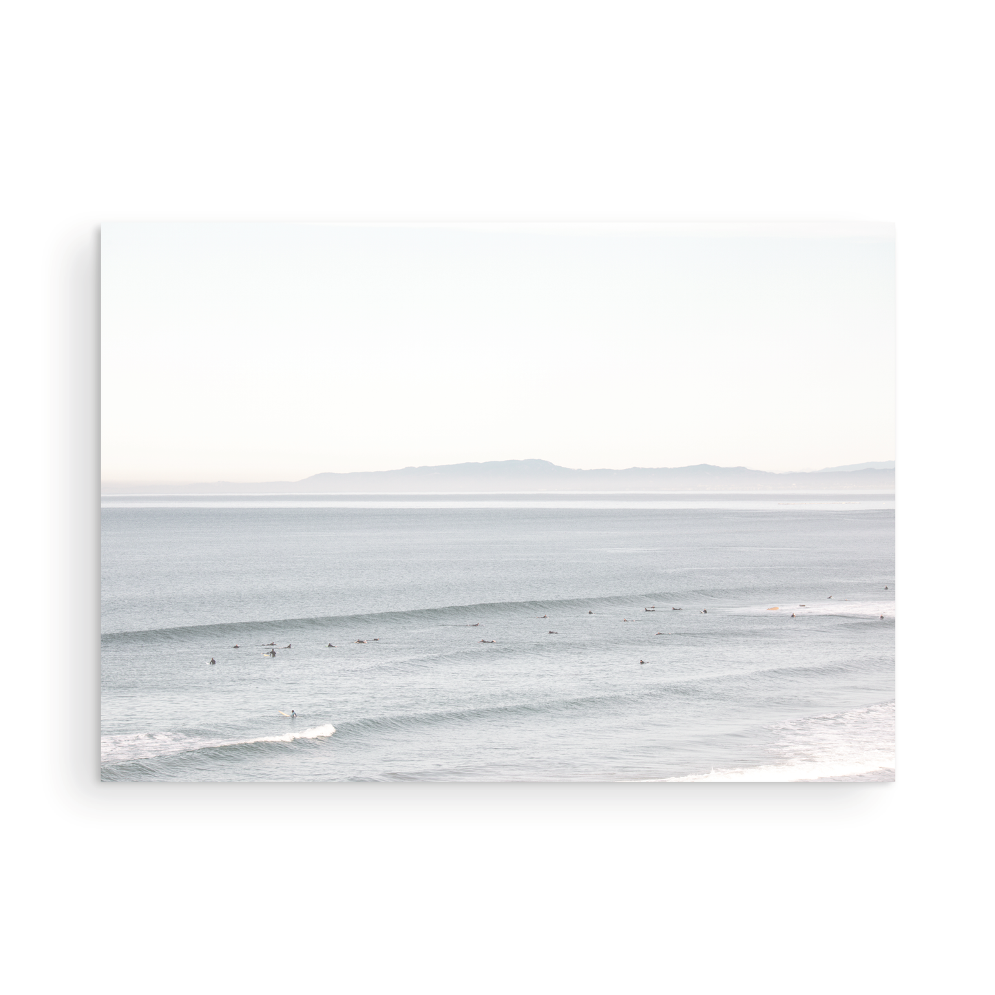 Coastal photography featuring a calm ocean scene with gentle waves and a hazy horizon line, predominantly in blue and white tones. Photograph in minimalist mock up.