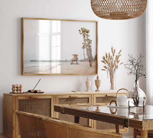 A wide landscape coastal photography view of San Clemente State Beach in Southern California, featuring a row of tall palm trees, a lifeguard tower, and people enjoying the calm beach. This image evokes Summer Vibes Wall Art and tropical beach print aesthetics. Photograph in minimalist mock up.