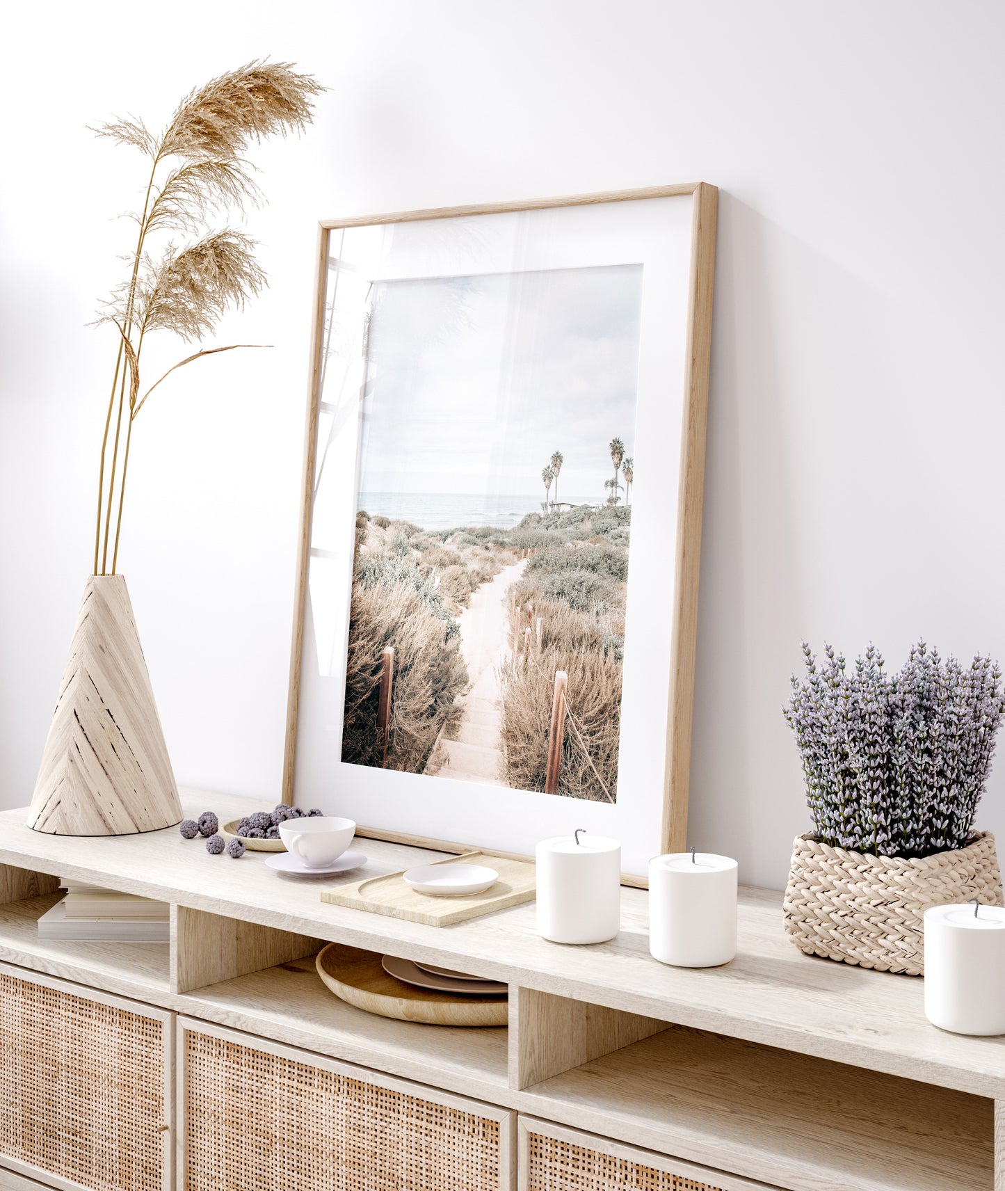 Minimalist vertical beach print showcasing the San Diego Sunset Cliffs, a sandy pathway with rustic wooden steps leading through coastal dune grass towards a calm ocean. This pastel beach art, evocative of the Southern California coastline, features a bright hazy sky and distant palm trees. A tranquil piece of travel photography, ideal for coastal wall art. Photograph in minimalist framed mock up.