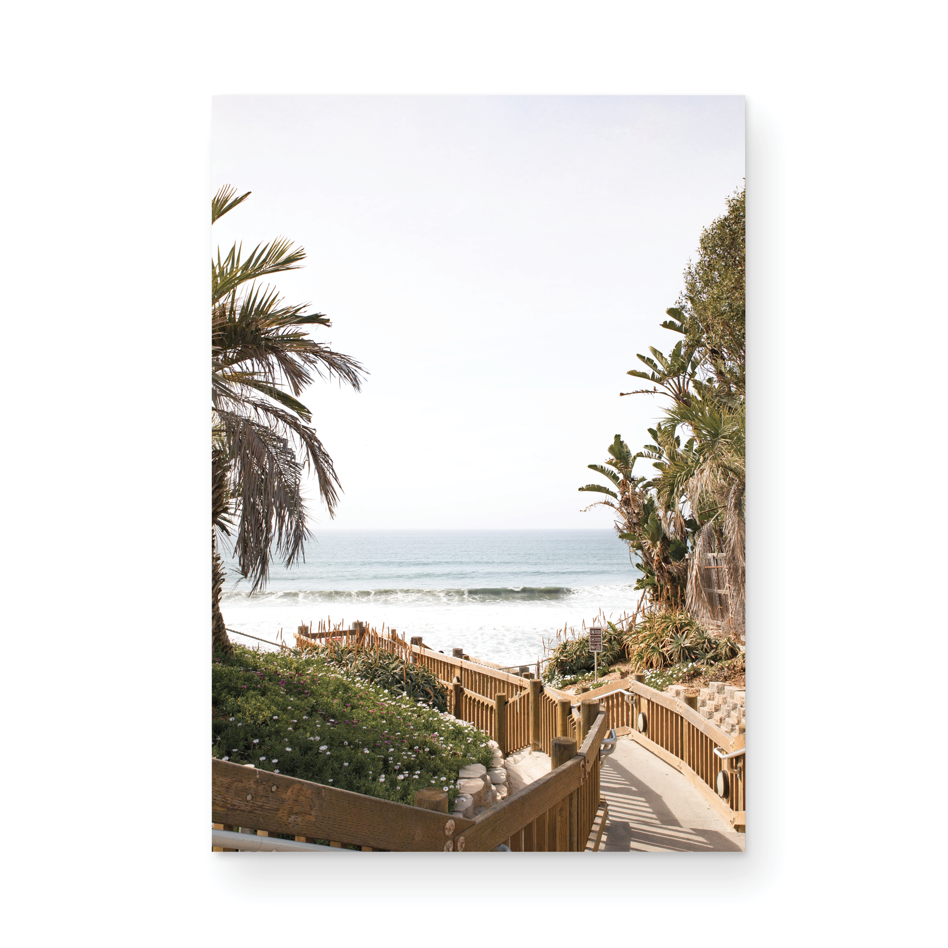Vertical coastal wall print featuring a stairway leading down to a beach with palm trees and ocean view. Photograph in minimalist mock up.