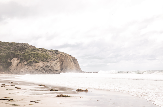 Minimalist ocean print of ocean waves and large sandy cliffs in the distance overlooking the seascape.