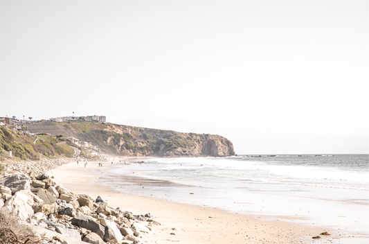 Minimalist ocean print of ocean waves with beach goers in the distance and large  sandy cliffs in the distance overlooking the seascape. Photograph in minimalist mock up.