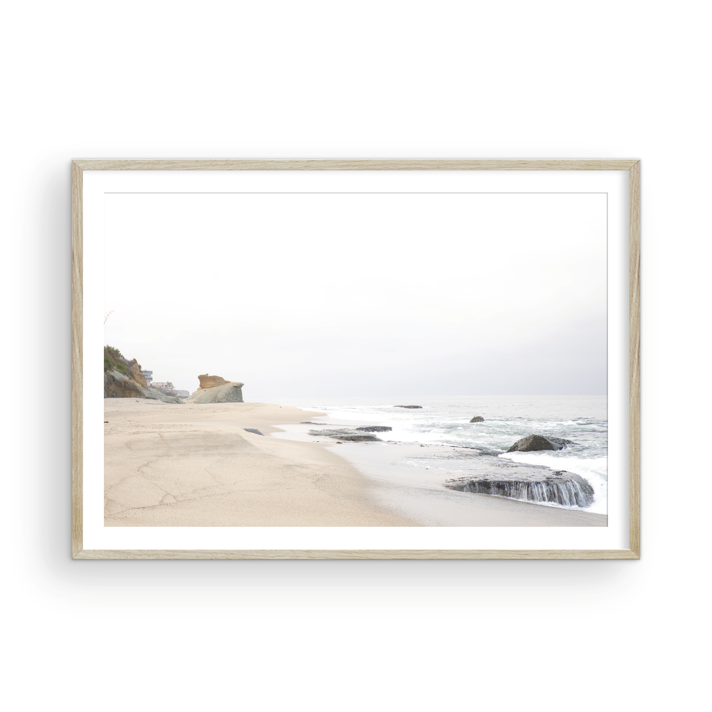 Horizontal coastal photography featuring a beach scene with calm ocean waves and a white sky, with rocks in the distance, located in Laguna California. Photograph in minimalist mock up.
