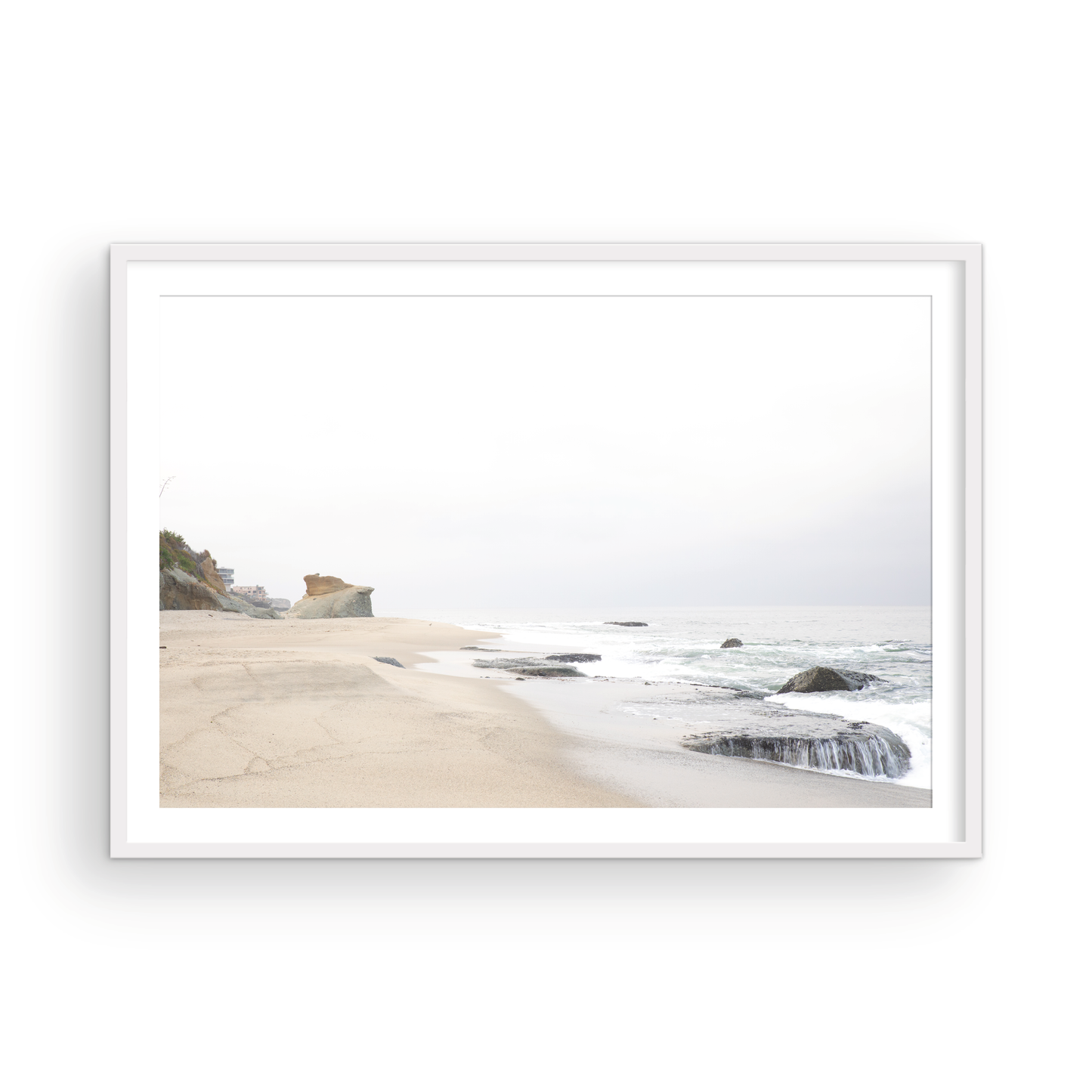 Horizontal coastal photography featuring a beach scene with calm ocean waves and a white sky, with rocks in the distance, located in Laguna California. Photograph in minimalist mock up.