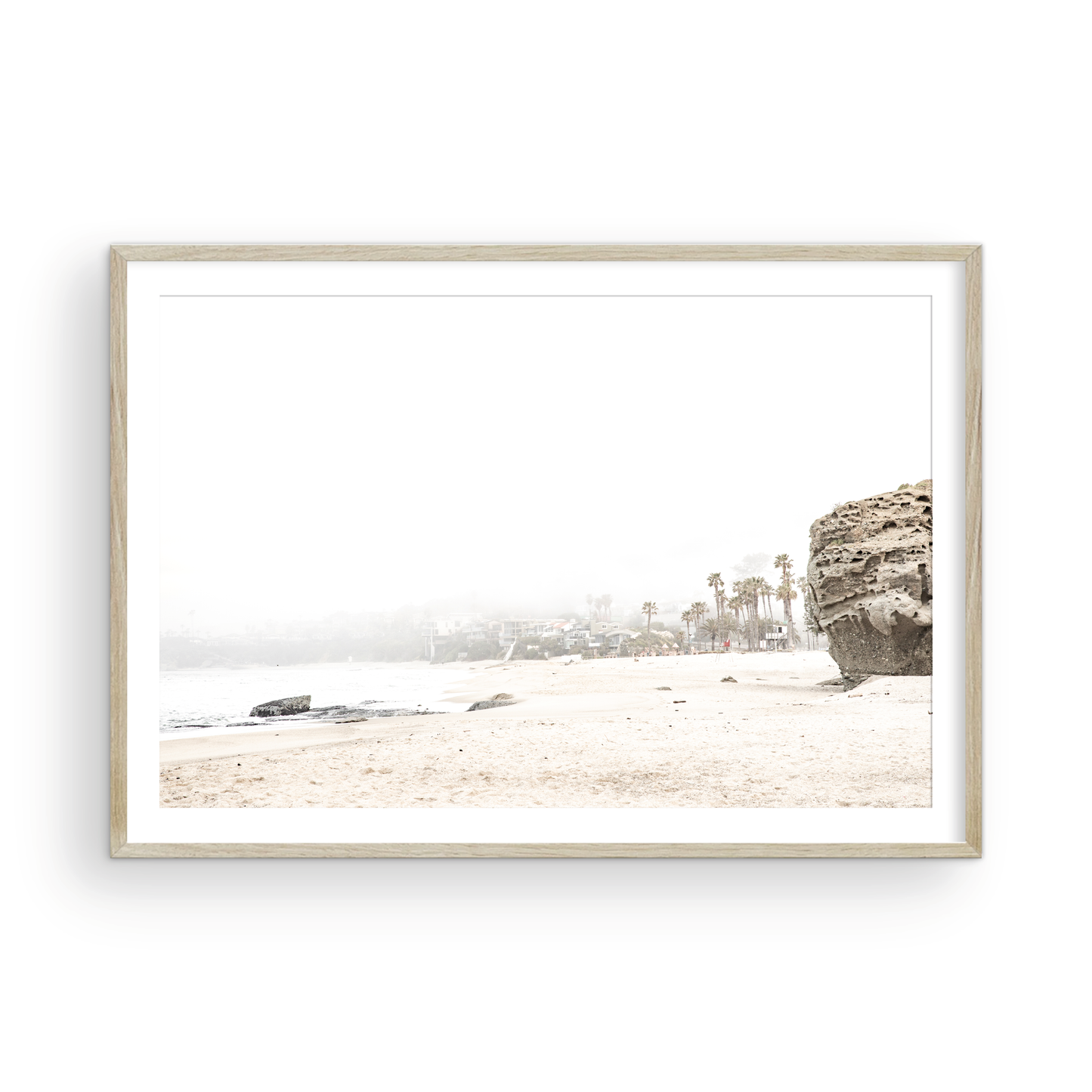 Horizontal coastal photography featuring a beach scene with a calm ocean and a rocky shore, beach homes in the foggy distance, located in Laguna California. Photograph in minimalist mock up.