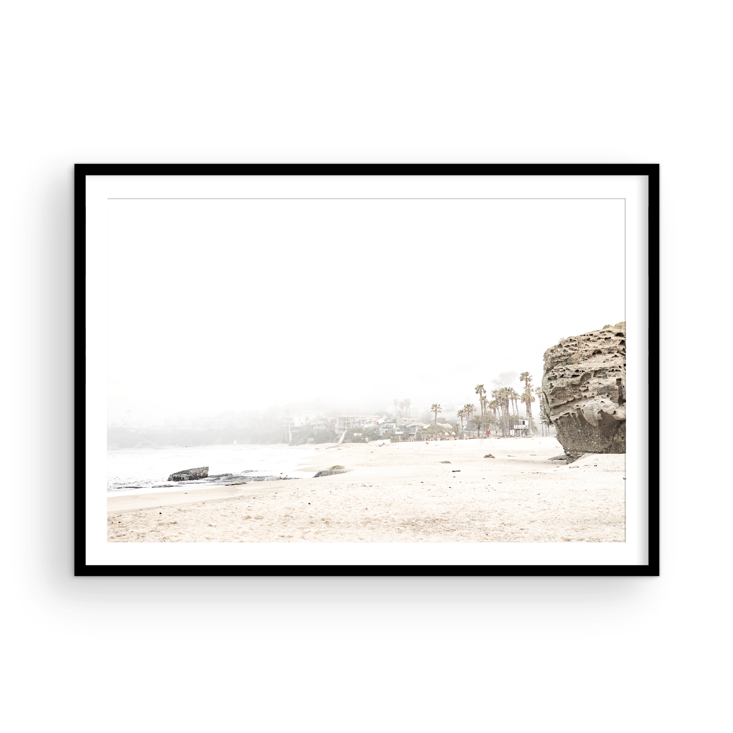 Horizontal coastal photography featuring a beach scene with a calm ocean and a rocky shore, beach homes in the foggy distance, located in Laguna California. Photograph in minimalist mock up.