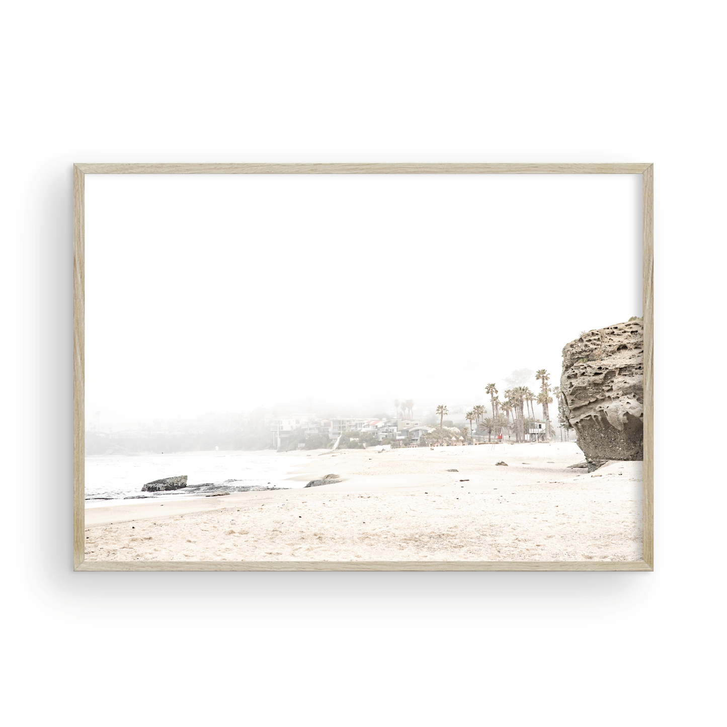 Horizontal coastal photography featuring a beach scene with a calm ocean and a rocky shore, beach homes in the foggy distance, located in Laguna California. Photograph in minimalist mock up.