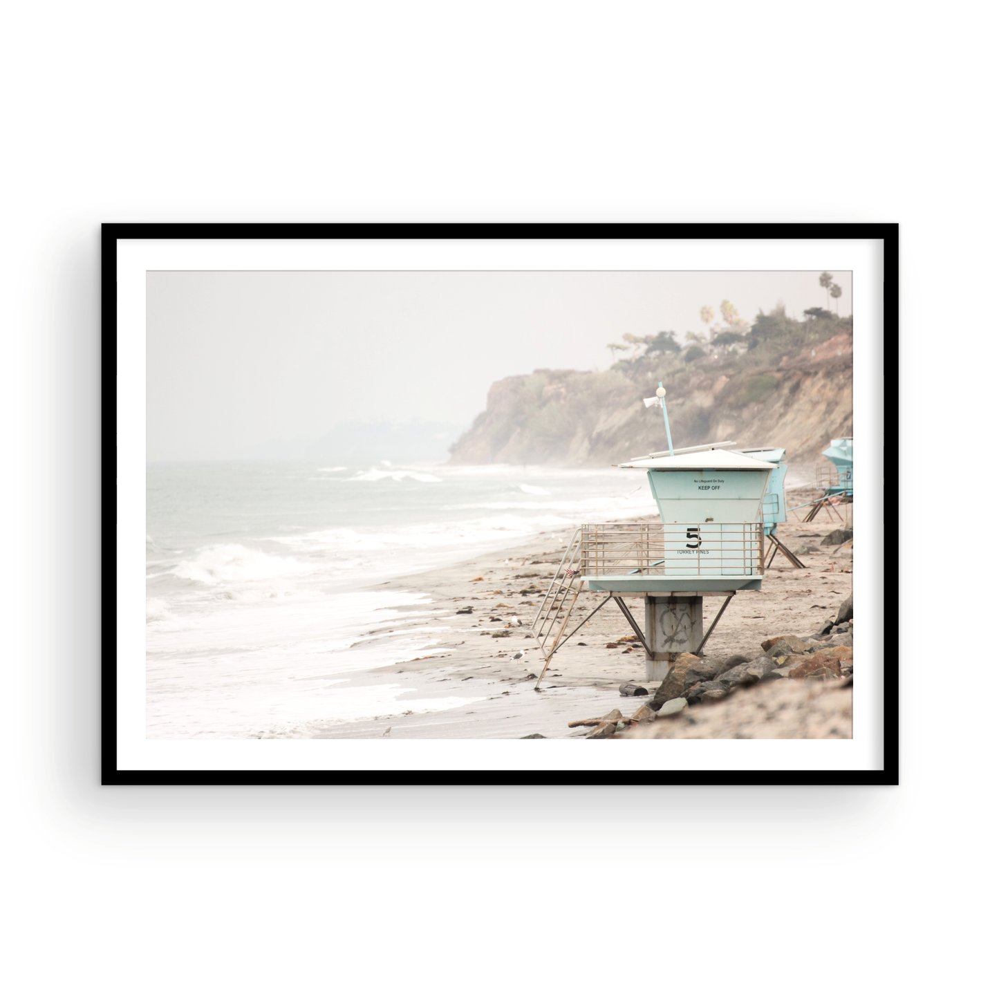 A serene piece of beach photography showcasing a light blue lifeguard tower, number 5, on the San Diego coast. This pastel beach art captures the iconic tower standing on wet sand with gentle ocean waves receding, under a hazy, overcast sky with distant cliffs. A perfect landscape lifeguard tower print for coastal theme wall art. Photograph in minimalist surf art mock up.