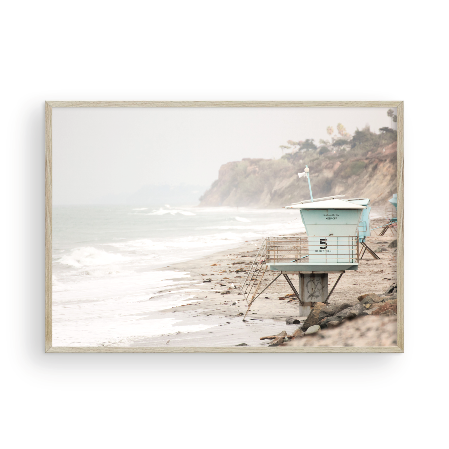 A serene piece of beach photography showcasing a light blue lifeguard tower, number 5, on the San Diego coast. This pastel beach art captures the iconic tower standing on wet sand with gentle ocean waves receding, under a hazy, overcast sky with distant cliffs. A perfect landscape lifeguard tower print for coastal theme wall art. Photograph in minimalist surf art mock up.