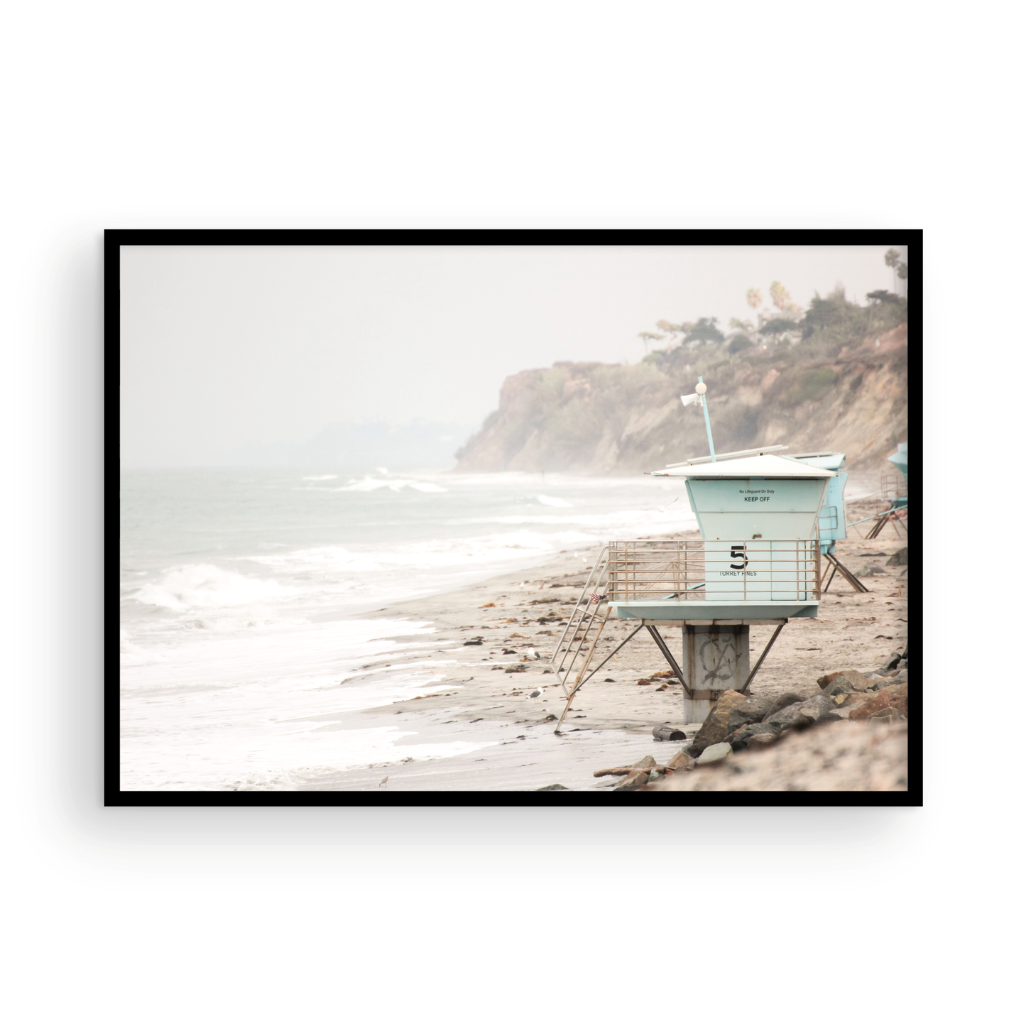 A serene piece of beach photography showcasing a light blue lifeguard tower, number 5, on the San Diego coast. This pastel beach art captures the iconic tower standing on wet sand with gentle ocean waves receding, under a hazy, overcast sky with distant cliffs. A perfect landscape lifeguard tower print for coastal theme wall art. Photograph in minimalist surf art mock up.