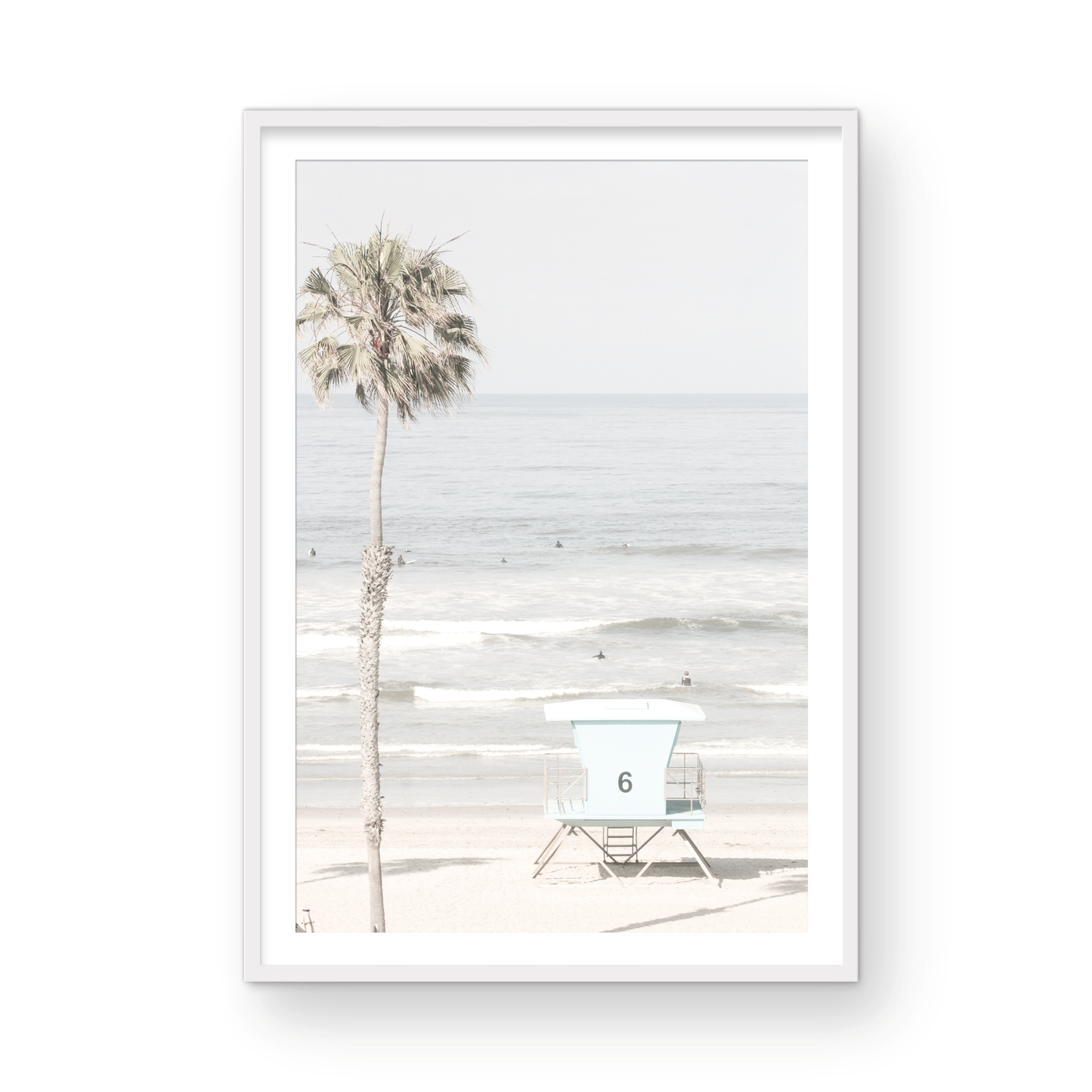 Dreamy coastal palm tree print featuring a tall palm tree with shaggy trunks in the foreground and a pastel blue lifeguard tower centered in the distance. This vertical tropical print is captured at Oceanside Beach on the Southern California coast, is bathed in bright, hazy sunlight, creating a pastel beach art effect. Photograph in minimalist mock up.