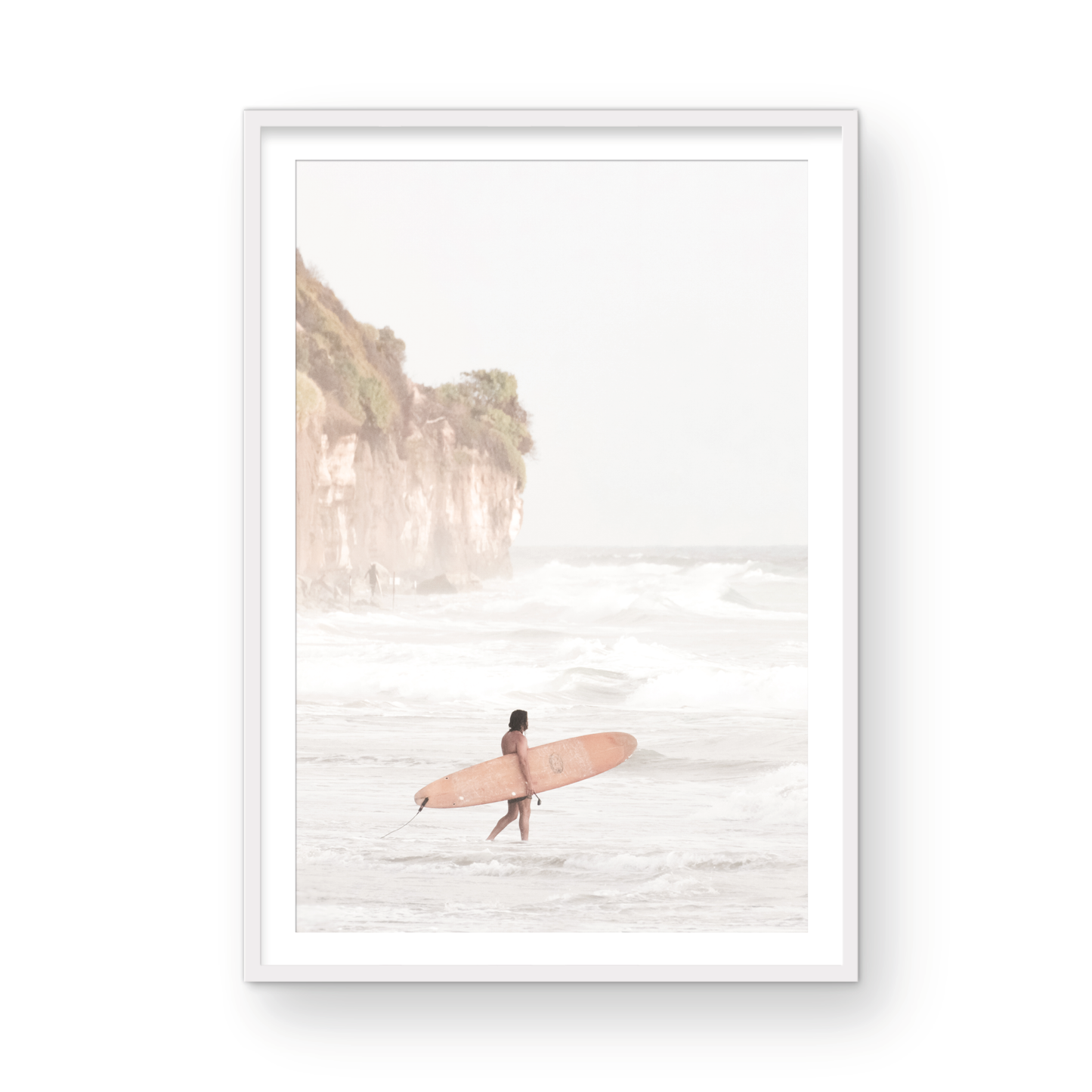 Vertical surf art print of a lone surfer carrying a surfboard, walking on a rocky, foggy shoreline at Moonlight State Beach with a lifeguard tower and cliff in the background. Photograph in minimalist mock up.