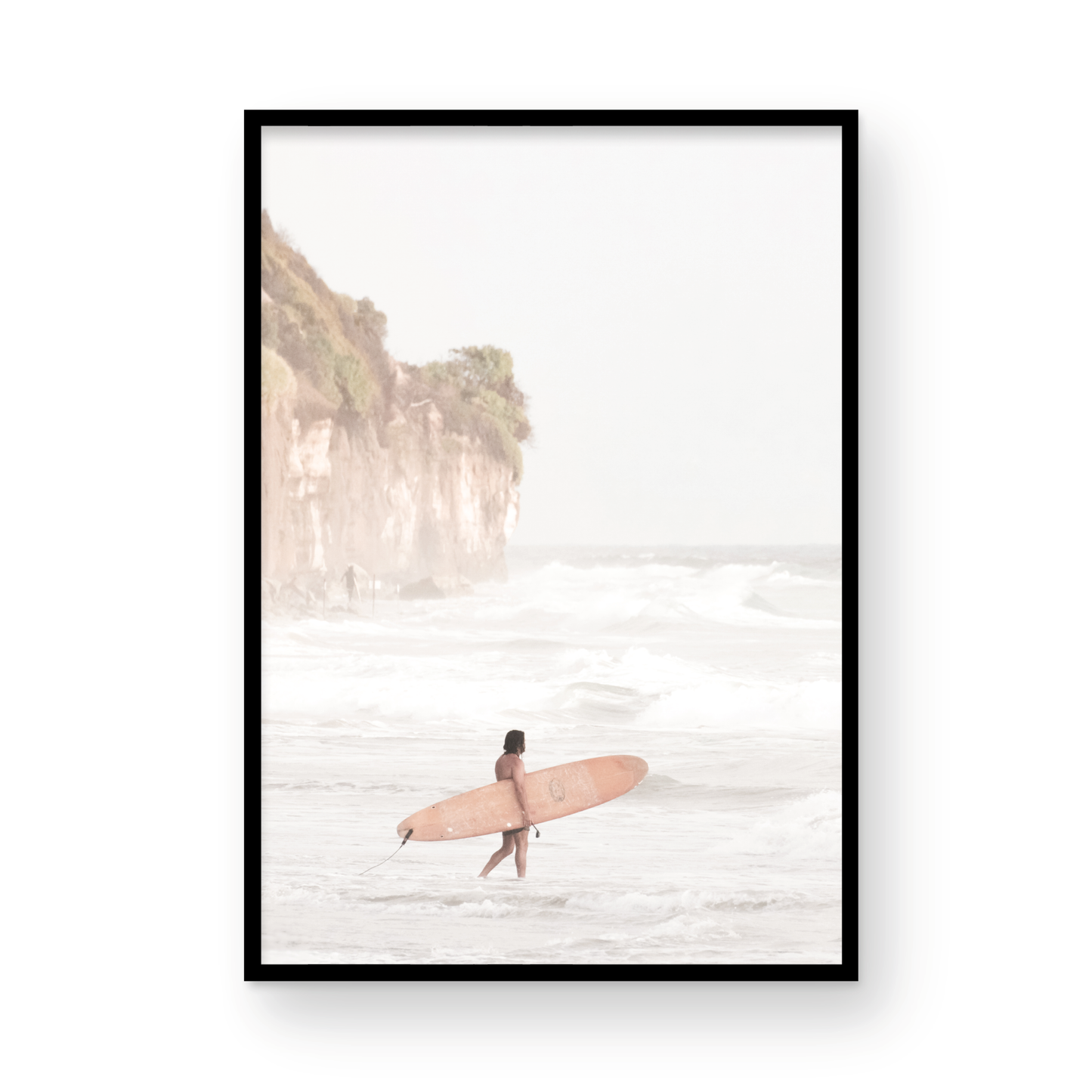 Vertical surf art print of a lone surfer carrying a surfboard, walking on a rocky, foggy shoreline at Moonlight State Beach with a lifeguard tower and cliff in the background. Photograph in minimalist mock up.