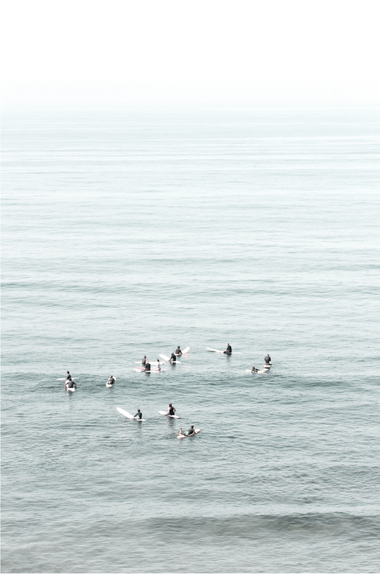 Vertical surf art showing multiple surfers waiting in the calm ocean water for waves, with a hazy Southern California coastline in the distance. This minimalist surf print captures authentic surf vibes.