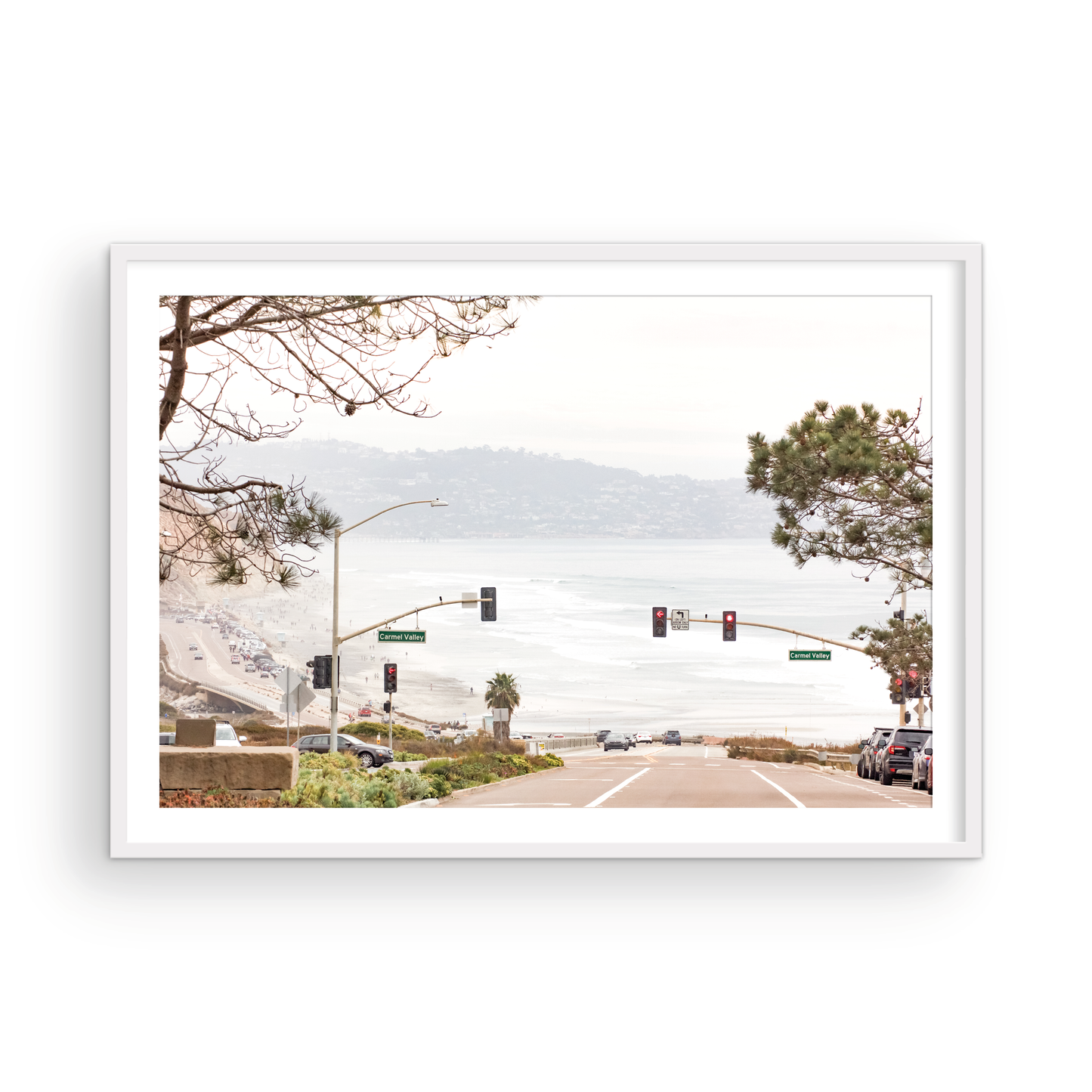 A hazy eye-level shot of San Diego Streets looks down a sloping road featuring red traffic lights and "Carmel Valley" signs, capturing a Local Surf Print vibe. The foreground of this California Wall Art showcases landscape and cars, framed by tree branches at the top, adding to the San Diego Photo aesthetic. The lighting suggests a daytime, perfect for Minimalist Beach Wall Art. This horizontal San Diego print makes a great piece of horizontal beach wall decor. Photograph in minimalist mock up
