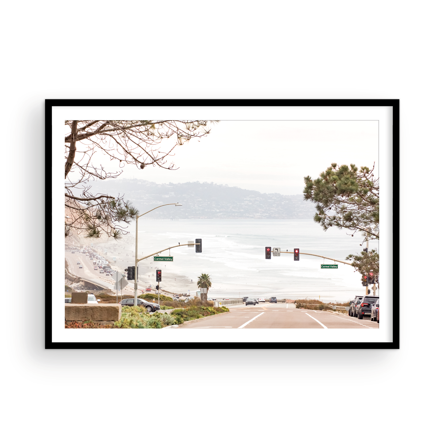 A hazy eye-level shot of San Diego Streets looks down a sloping road featuring red traffic lights and "Carmel Valley" signs, capturing a Local Surf Print vibe. The foreground of this California Wall Art showcases landscape and cars, framed by tree branches at the top, adding to the San Diego Photo aesthetic. The lighting suggests a daytime, perfect for Minimalist Beach Wall Art. This horizontal San Diego print makes a great piece of horizontal beach wall decor. Photograph in minimalist mock up
