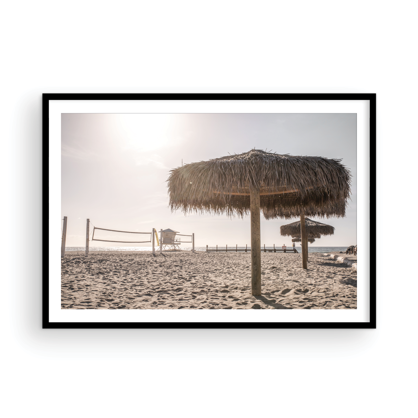 Landscape coastal photography capturing a thatched beach umbrella on a sandy beach, volleyball nets and a lifeguard tower in the distance, with ocean views on the horizon. Photograph in minimalist mock up.