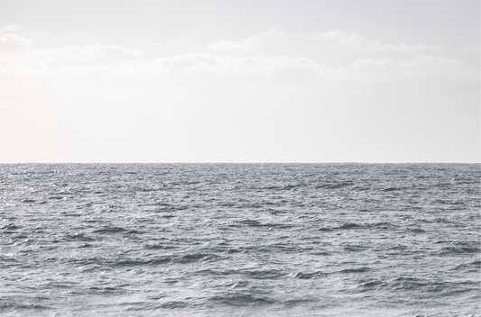 Minimalist ocean print of gentle ocean waves rolling at Moonlight Beach, San Diego, under a bright, soft sky. This calm beach print provides a serene seascape.