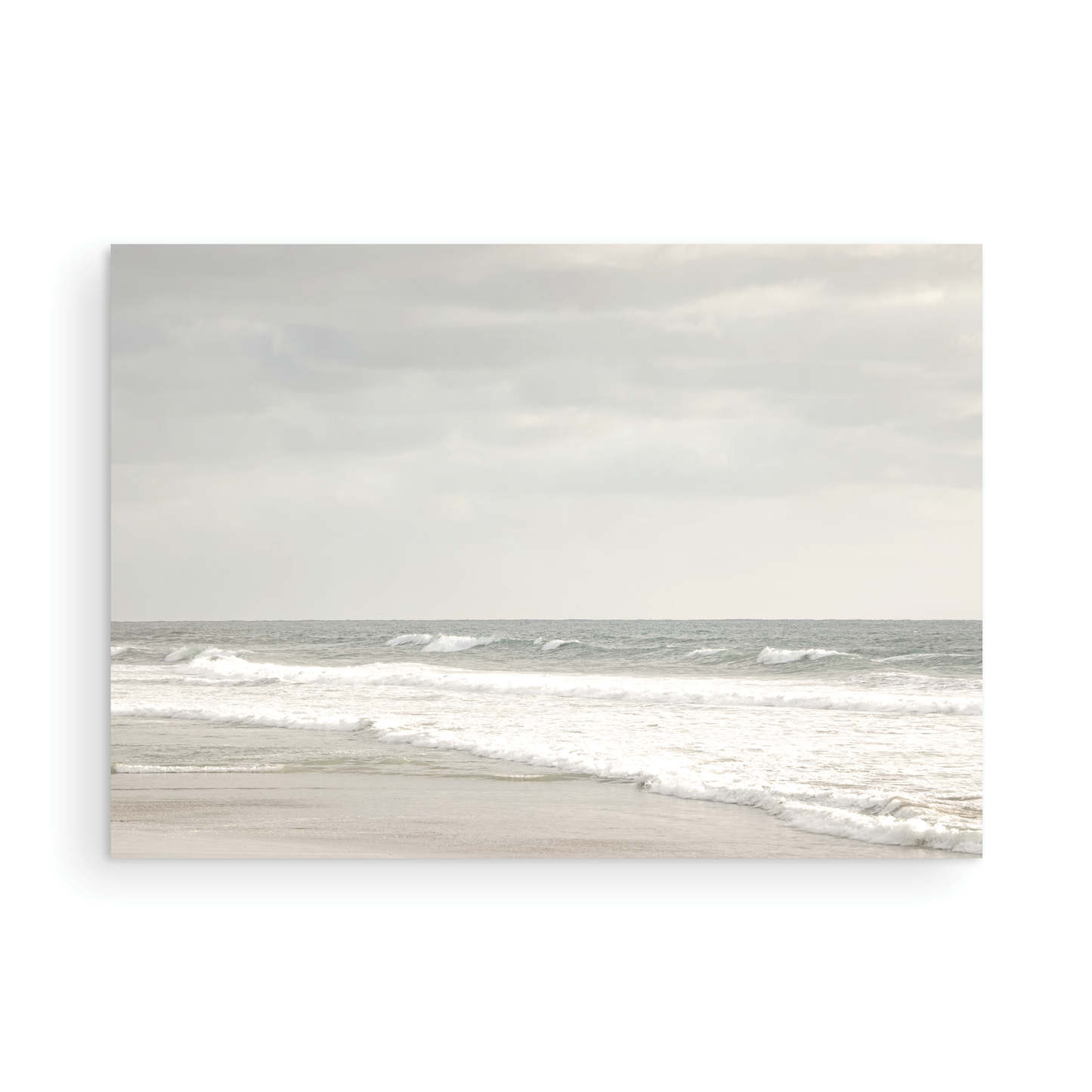 Horizontal minimalist ocean print of gentle ocean waves rolling onto a sandy shoreline at Moonlight Beach, San Diego, under a bright, soft sky. This calm beach print provides a serene seascape. Photograph in minimalist mock up.