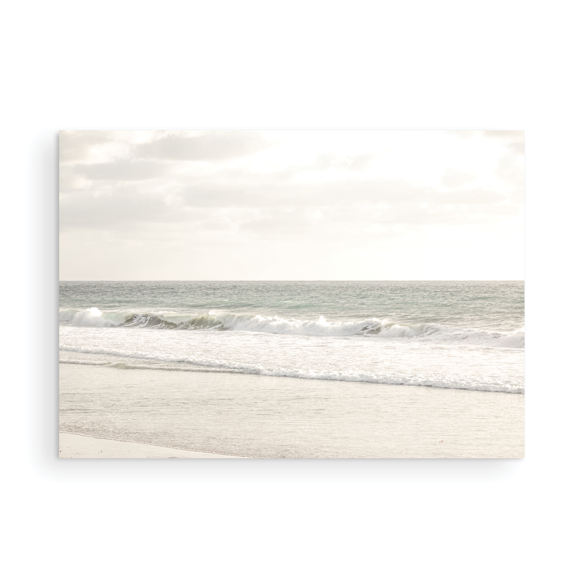 Minimalist ocean print of gentle ocean waves rolling onto a sandy shoreline at Moonlight Beach, San Diego, under a bright, soft sky. This calm beach print provides a serene seascape. Photograph in minimalist mock up.