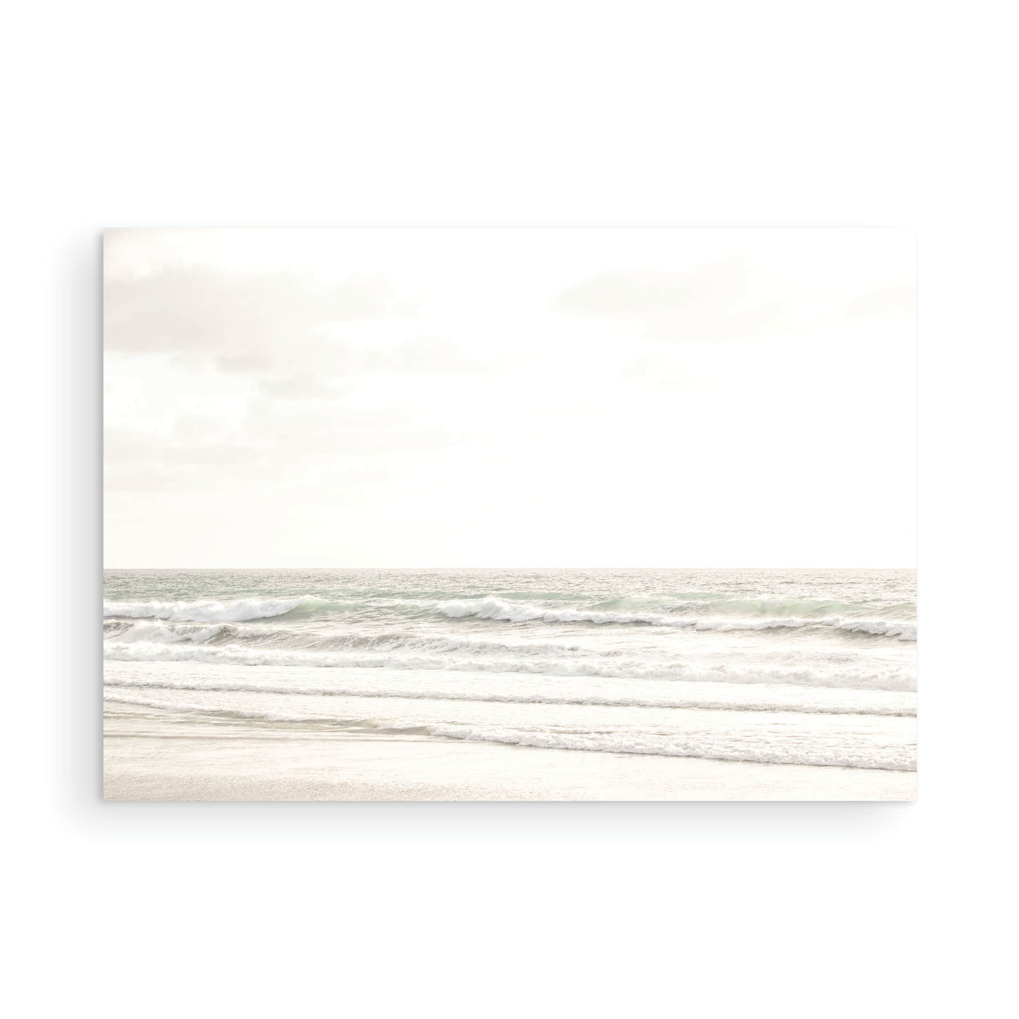 Horizontal minimalist ocean print of gentle ocean waves rolling onto a sandy shoreline at Moonlight Beach, San Diego, under a bright, soft sky. This calm beach print provides a serene seascape. Photograph in minimalist mock up.