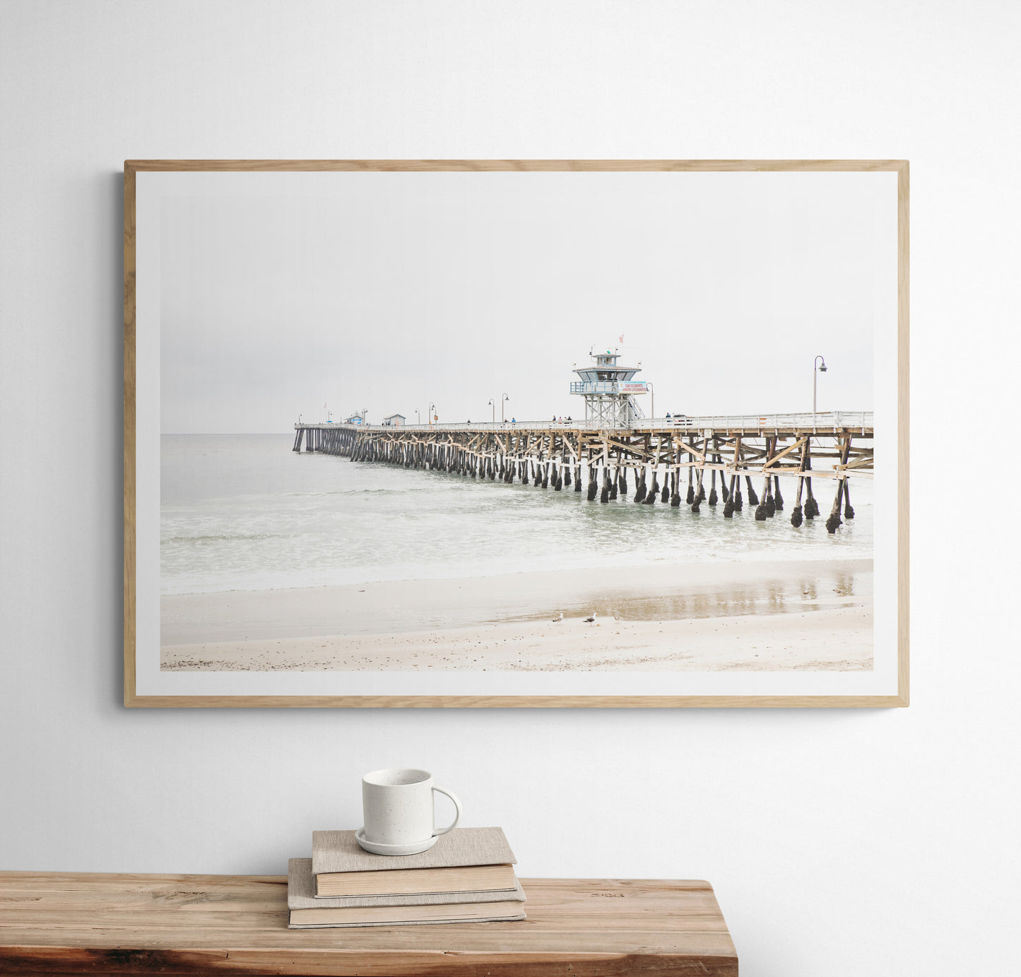 A long wooden pier, the San Clemente Pier, extends into the ocean in this landscape coastal photography. The beach in the foreground suggests a calm ocean print, ideal for a large coastal wall art or a beach cottage wall decor. Photograph in minimalist mock up.