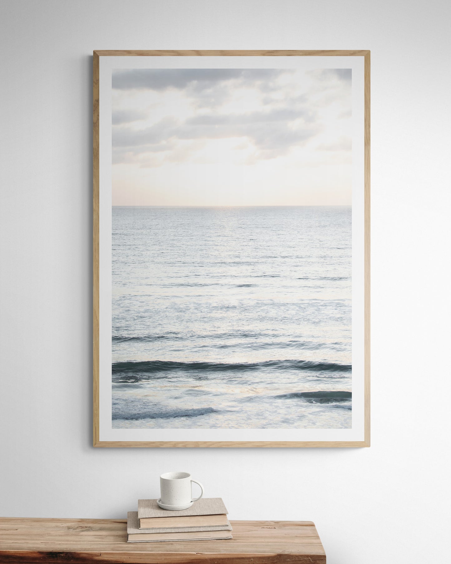 Fine art of vertical landscape print by Southern California photographer Kim Dybczak of Salt Creek Prints, featuring a bright image capturing pale blue ocean waves, light gray clouds in a bright sky. Gentle, small waves in the near and far distance. The sky is a uniform, pale white, creating a soft, overcast atmosphere. Photograph in framed minimalist mock up