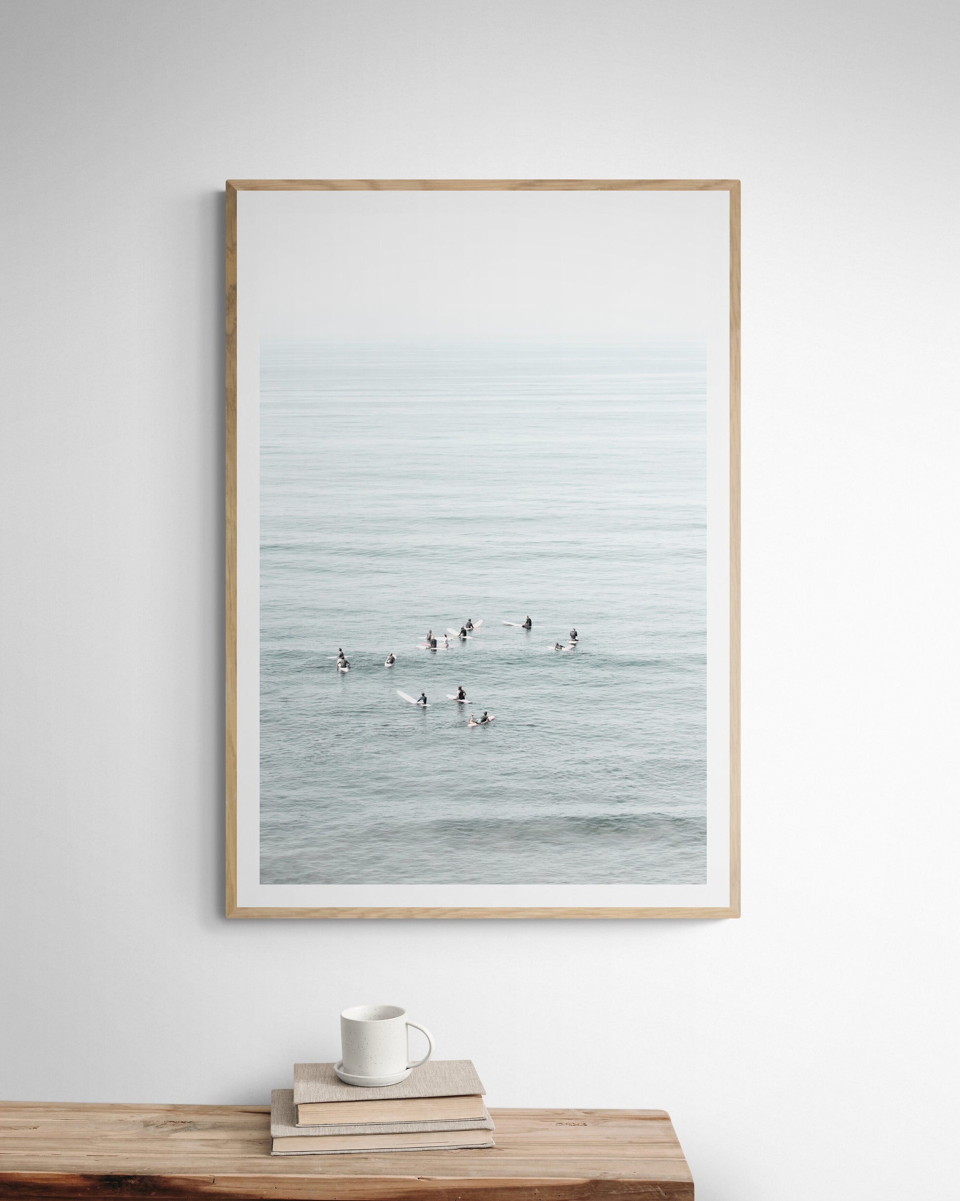 Vertical surf art showing multiple surfers waiting in the calm ocean water for waves, with a hazy Southern California coastline in the distance. This minimalist surf print captures authentic surf vibes. Photograph in minimalist mock up.