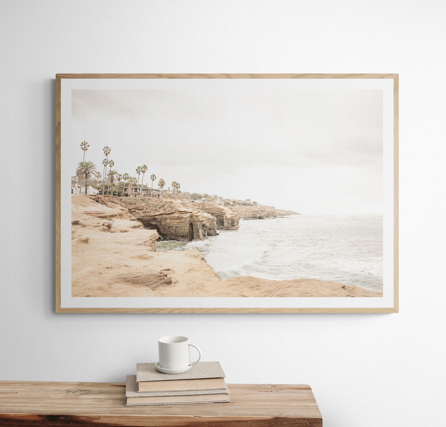 Fine art of Sunset Cliffs, San Diego California horizontal print of hazy high-angle landscape beach photography captures a light blue ocean meeting tall tan, brown cliffs rise as iconic coastal scenery. Photograph in minimalist mock up.