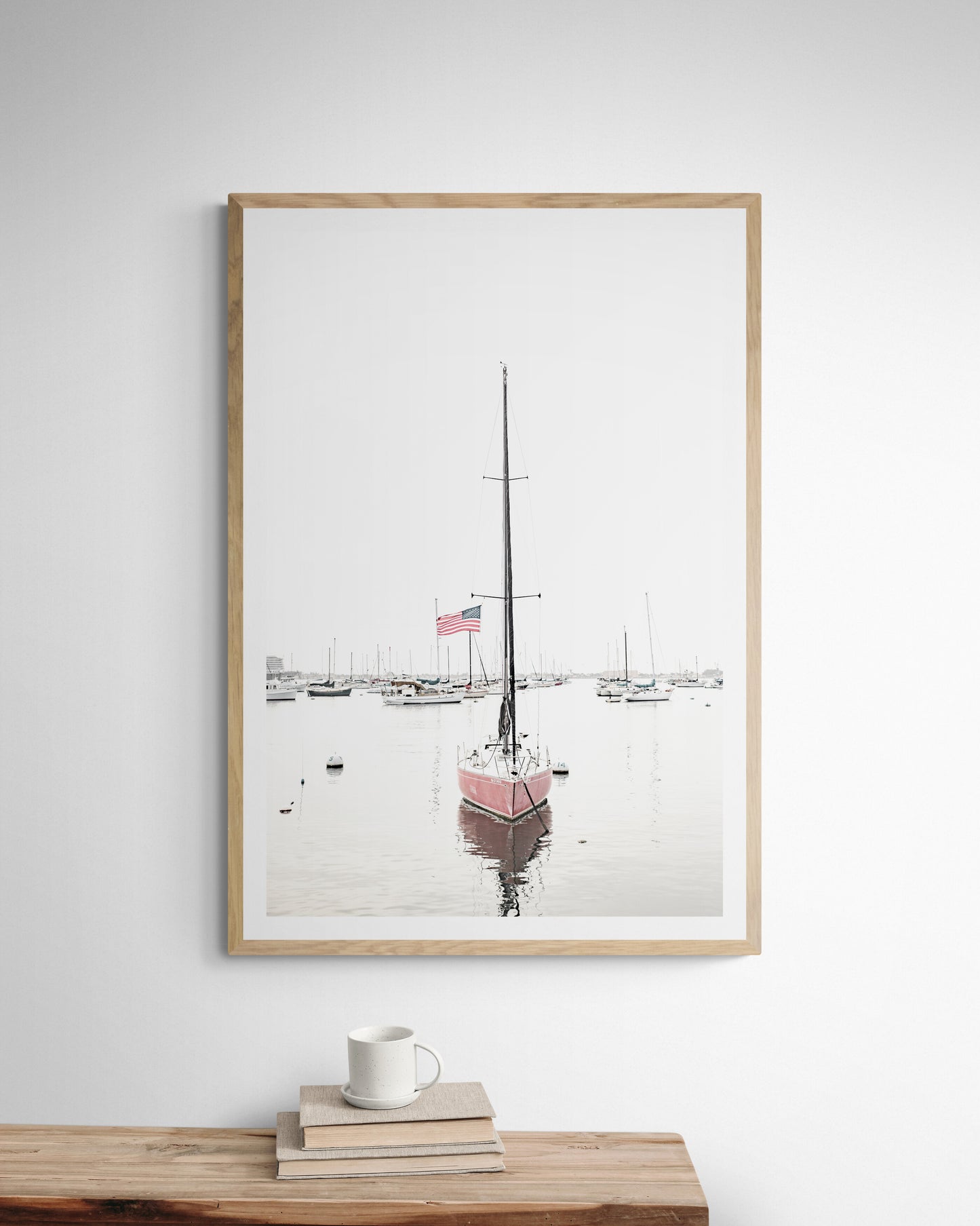 A vertical San Diego print featuring a lone red sailboat with an American flag, anchored in a calm San Diego harbor. This minimalist ocean print captures the essence of coastal photography and is perfect for modern coastal decor. Photograph in minimalist mock up.