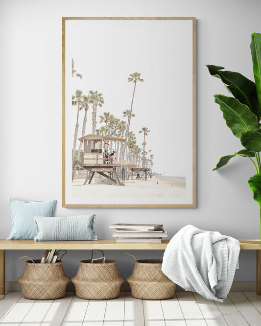 A landscape coastal photography view of San Clemente State Beach in Southern California, featuring a row of tall palm trees, a lifeguard tower, and people enjoying the calm beach. This vertical image evokes Summer Vibes Wall Art and tropical beach print aesthetics. Photograph in minimalist mock up.