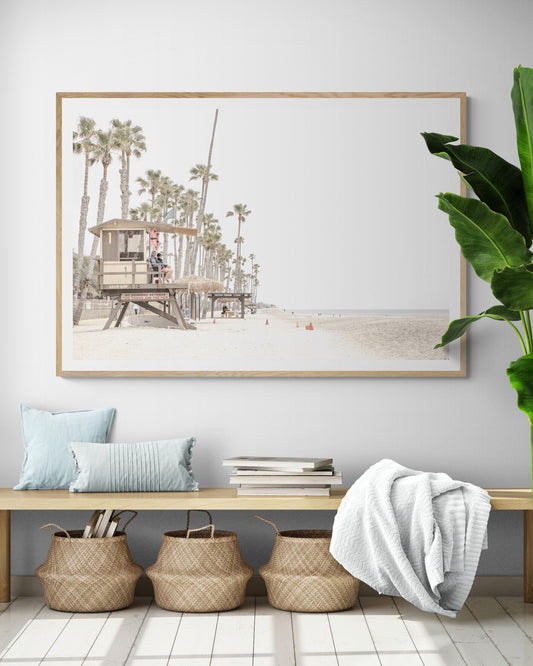 A wide landscape coastal photography view of San Clemente State Beach in Southern California, featuring a row of tall palm trees, a lifeguard tower, and people enjoying the calm beach. This image evokes Summer Vibes Wall Art and tropical beach print aesthetics. Photograph in minimalist mock up.