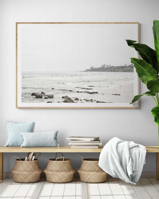 Landscape coastal photography of Salt Creek Beach with dark rocks on the shore and numerous surfers in the ocean. A neutral ocean print perfect for beach house decor. Photograph in minimalist mock up.