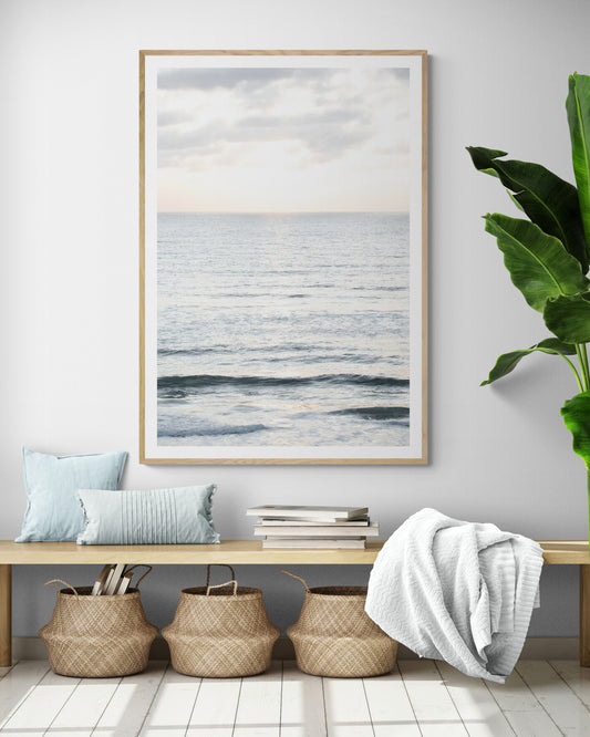 Fine art of vertical landscape print by Southern California photographer Kim Dybczak of Salt Creek Prints, featuring a bright image capturing pale blue ocean waves, light gray clouds in a bright sky. Gentle, small waves in the near and far distance. The sky is a uniform, pale white, creating a soft, overcast atmosphere. Photograph in framed minimalist mock up