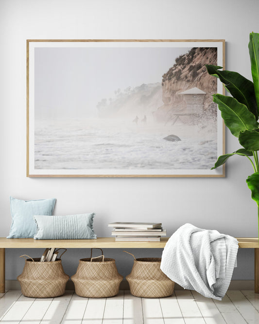 Hazy surf art of two surfers running into stormy ocean waves at Moonlight State Beach, with a lifeguard tower and cliff disappearing into the fog. A dramatic seascape print. Photograph in minimalist mock up