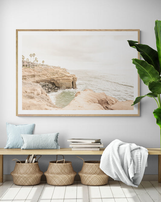 Fine art of Sunset Cliffs, San Diego California horizontal print of hazy high-angle landscape beach photography captures a light blue ocean meeting tall tan, rocky, brown cliffs rise as iconic coastal scenery. Photograph in minimalist mock up.