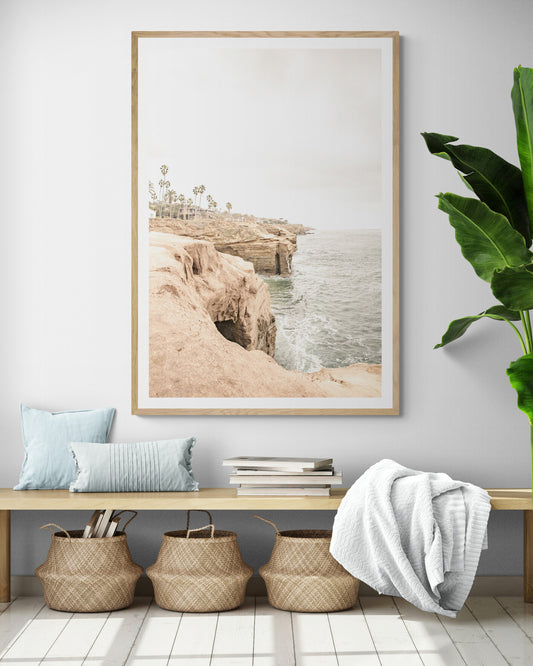 Fine art of Sunset Cliffs, San Diego California vertical print of hazy high-angle landscape beach photography captures a light blue ocean meeting tall tan, brown cliffs rise as iconic coastal scenery. Photograph in minimalist mock up.