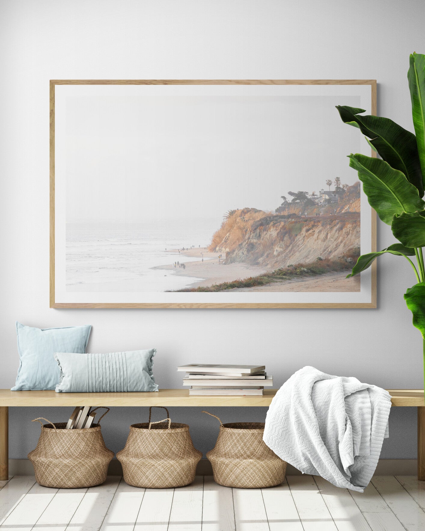 Fine art of Torrey Pines, San Diego California horizontal print of hazy high-angle landscape beach photography captures a light blue ocean meeting a sandy beach with many beach goers. To the right, tall tan and brown cliffs rise as iconic coastal scenery. Photograph in minimalist framed entry way mock up.