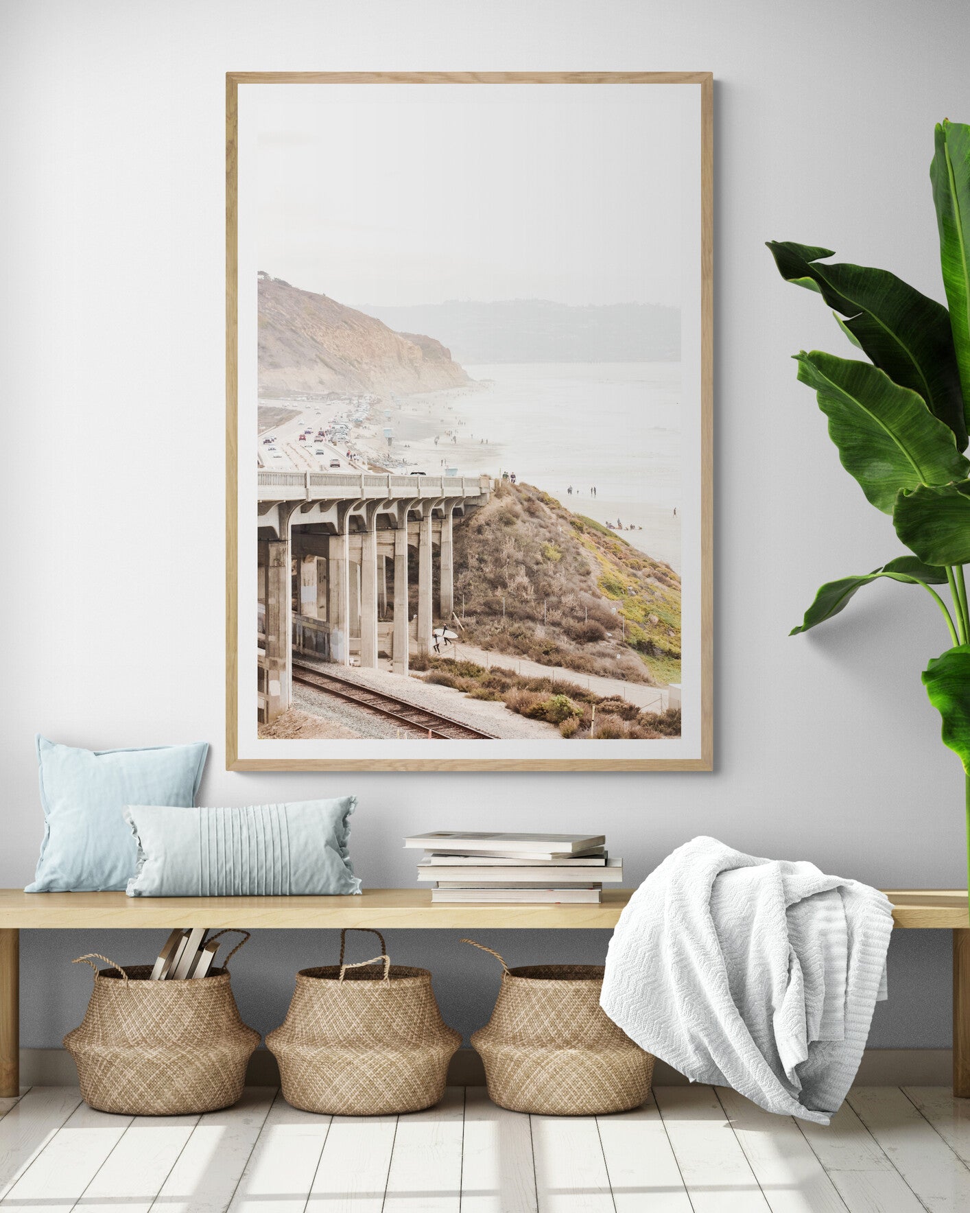 Captivating Torrey Pines San Diego coast scene, presented as vertical beach art. This piece of travel photography features a prominent bridge extending over a wide sandy beach with calm ocean waves. A coastal road winds along the base of rugged cliffs, with a lone coastal palm tree adding a touch of tropical essence to this Southern California seascape print. Photograph in minimalist entry way mock up